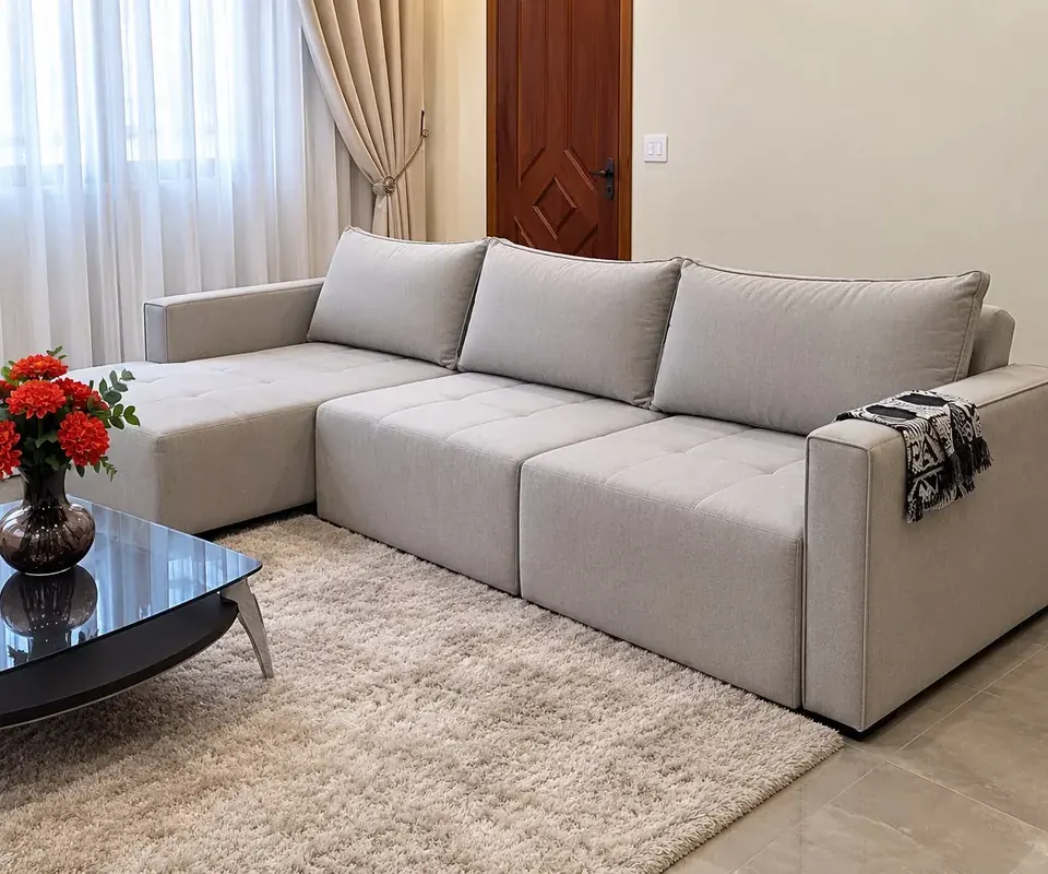 Sofá bege com chaise em uma sala com cortinas claras e flores vermelhas.